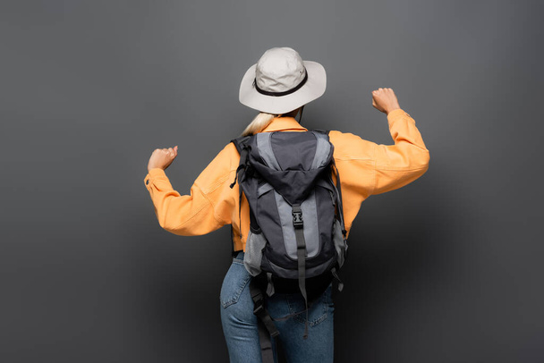 Vista trasera de turista con mochila mostrando sí gesto sobre fondo gris  - Foto, Imagen