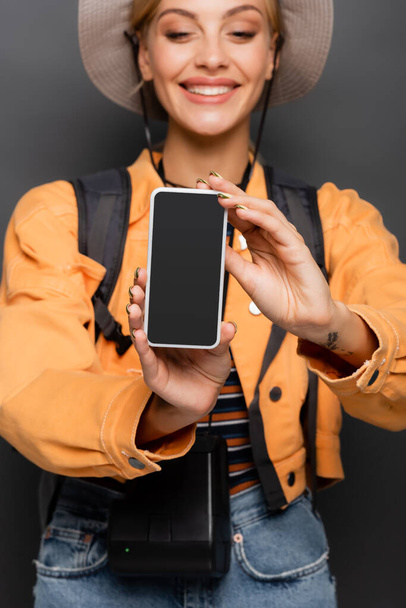Смартфон с чистым экраном в руках размытого веселого туриста на сером  - Фото, изображение