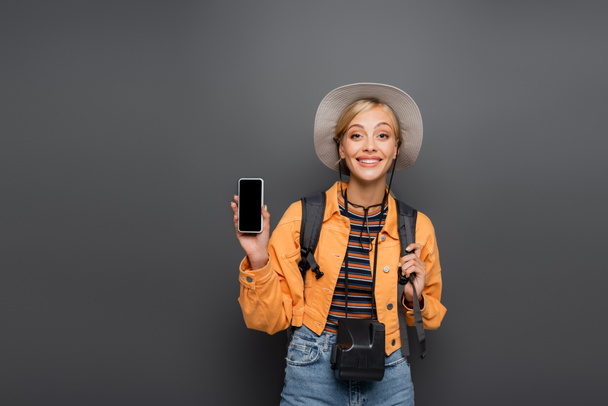 Smiling blonde tourist with smartphone and vintage camera isolated on grey  - Fotografie, Obrázek