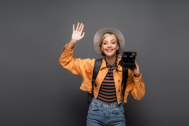 Positive tourist holding vintage camera and waving hand isolated on grey  - Zdjęcie, obraz