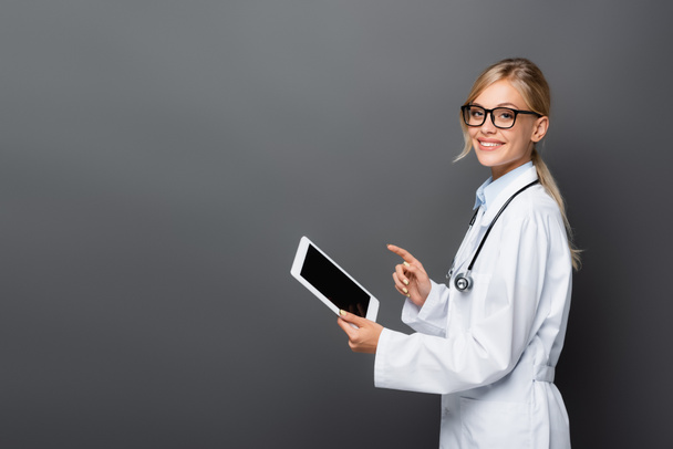 Positive doctor pointing at digital tablet with blank screen isolated on grey  - Photo, Image