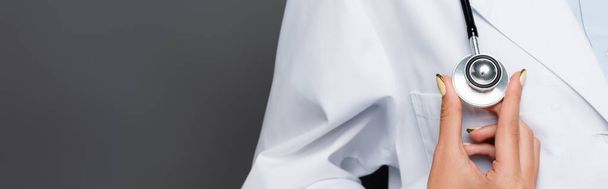 Vue recadrée du médecin en manteau blanc tenant le statoscope isolé sur gris, bannière  - Photo, image