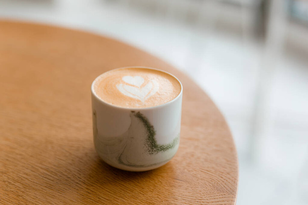 Een kopje cappuccino met latte art. Koffie in witte beker op bruine houten tafel in café. Concept van gemakkelijk ontbijt. - Foto, afbeelding