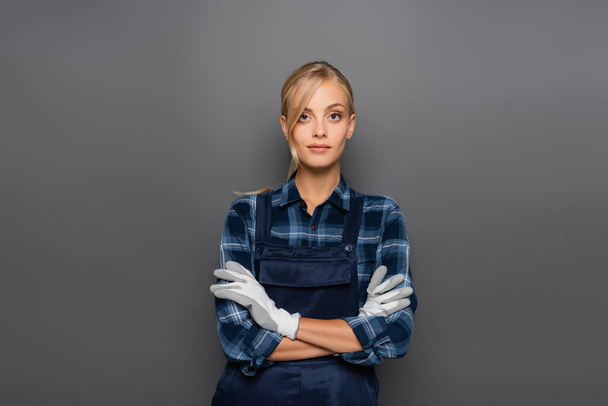 Blonde plumber in gloves standing with crossed arms isolated on grey  - Photo, Image