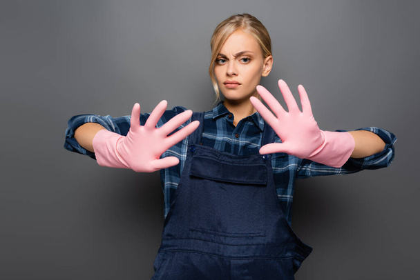 Verward loodgieter kijken naar handen in rubberen handschoenen op grijs  - Foto, afbeelding