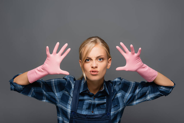 Disgusted plumber in rubber gloves gesturing and looking at camera isolated on grey  - Фото, зображення