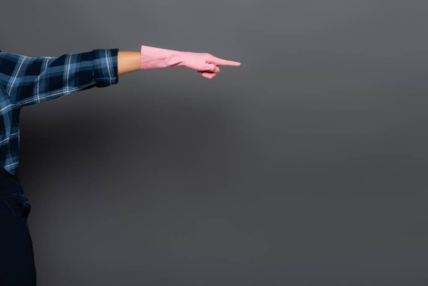 Vista recortada del joven fontanero en guante de goma apuntando con el dedo aislado en gris  - Foto, imagen