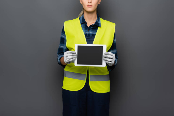 Ausgeschnittene Ansicht des Bauarbeiters in Warnweste und Handschuhen mit digitalem Tablet und leerem Bildschirm isoliert auf grau  - Foto, Bild
