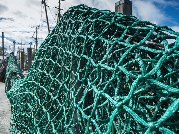 Nahaufnahme eines grünen Fischernetzes mit Fischerbootmasten im Hintergrund.  - Foto, Bild