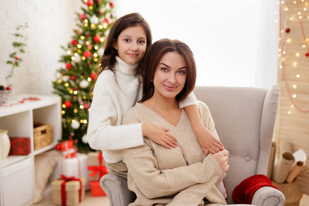 aile ve Noel konsepti - Mutlu anne ve tatlı kızın portresi Noel ağacıyla süslü bir odada oturuyor - Fotoğraf, Görsel