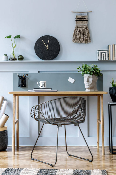 Stylish scandinavian living room interior with wooden desk, chair, wood panleing with shelf, table lamp, plants, black clock, office supplies and elegant accessories in modern home decor. - 写真・画像