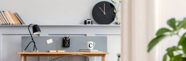Scandinavian home office interior with wooden desk, design chair, wood panleing with shelf, plant, table lamp, office supplies and elegant accessories in modern home decor. - Fotó, kép