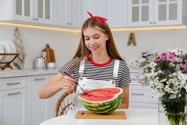Beautiful teenage girl eating half of watermelon with spoon in kitchen - Foto, immagini