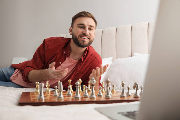 Young man playing chess with partner through online video chat on bed at home - Foto, Imagen