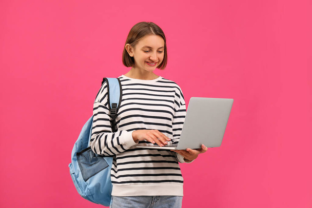 Young student with laptop and backpack on pink background - Foto, immagini