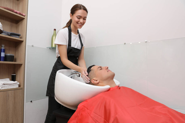 Professional hairdresser washing client's hair at sink in salon - 写真・画像