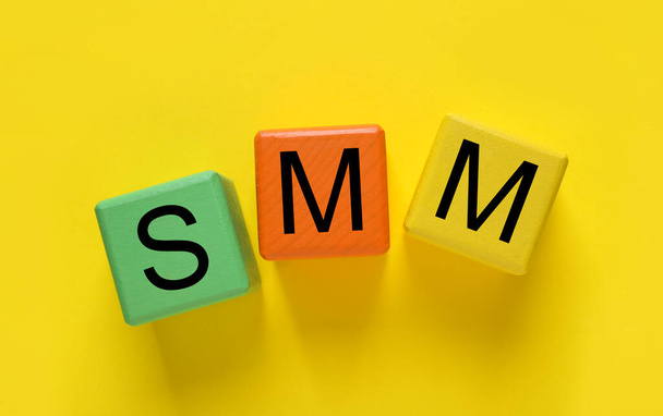 Colorful cubes with abbreviation SMM (Social media marketing) on yellow background, flat lay - Foto, Imagem