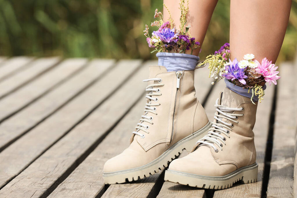Woman standing on wooden pier with flowers in socks outdoors, closeup. Space for text - Fotoğraf, Görsel