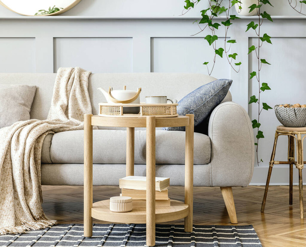 Scandinavian living room interior with design grey sofa, wooden coffee table, tropical plants, shelf, mirror, furniture, plaid pillow, teapot, book and elegant personal accessories in home decor. - Fotoğraf, Görsel