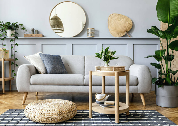 Scandinavian living room interior with design grey sofa, wooden coffee table, tropical plants, shelf, mirror, furniture, plaid pillow, teapot, book and elegant personal accessories in home decor. - Foto, Imagen