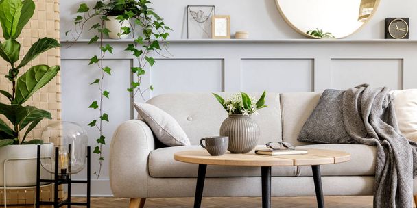Scandinavian living room interior with design grey sofa, wooden coffee table, tropical plants, shelf, mirror, furniture, plaid pillow, teapot, book and elegant personal accessories in home decor. - Foto, afbeelding