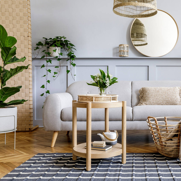 Scandinavian living room interior with design grey sofa, wooden coffee table, tropical plants, shelf, mirror, furniture, plaid pillow, teapot, book and elegant personal accessories in home decor. - Foto, afbeelding