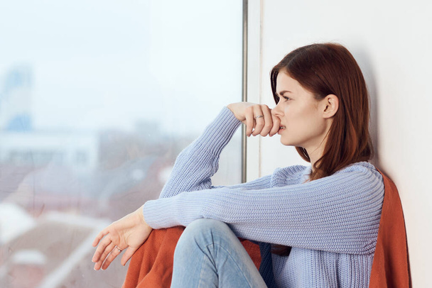 woman with sad expression sits by the window with a plaid - Foto, afbeelding