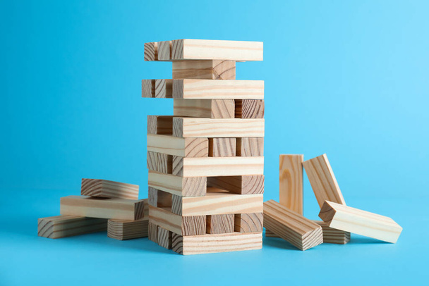 Jenga tower made of wooden blocks on light blue background - Foto, Imagem