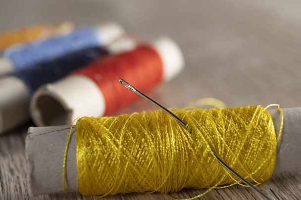 Un ago in fili gialli su uno sfondo di legno chiaro. Filati tessili colorati per cucire sul tavolo. - Foto, immagini