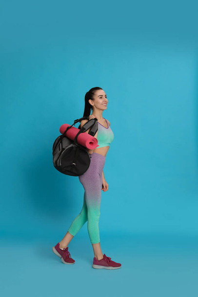 Beautiful woman with sports bag and yoga mat on light blue background - Fotografie, Obrázek