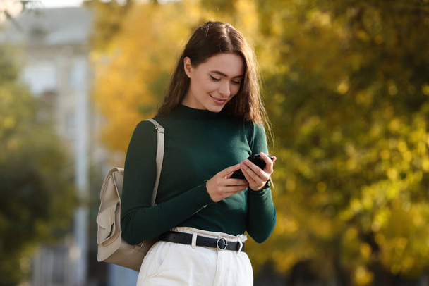Giovane donna con elegante zaino beige e smartphone nel parco - Foto, immagini