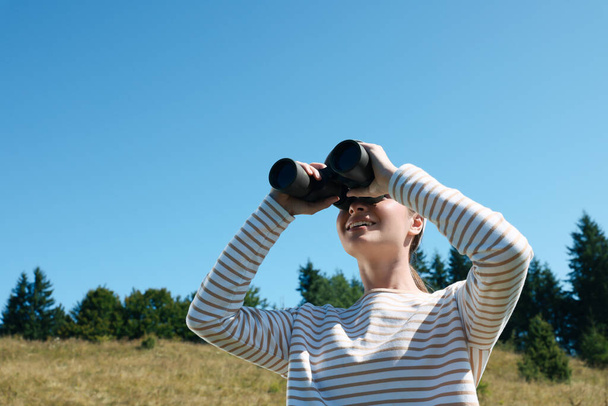Woman looking through binoculars outdoors on sunny day - Фото, изображение
