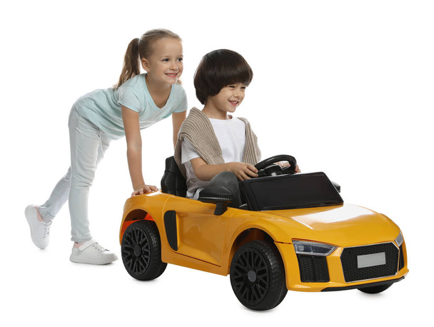 Cute girl pushing children's electric toy car with little boy on white background - Фото, изображение