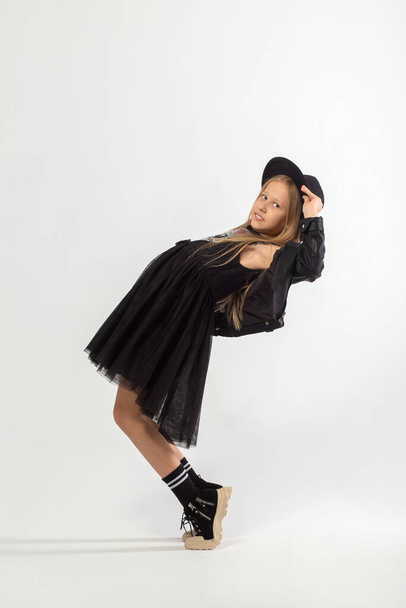 A full-length portrait of dancing young girl with long brown hair dressed in a hooligan style on white background in studio. - Photo, image