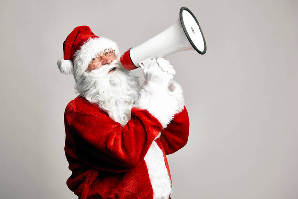 Caucasian Santa Claus talking by megaphone on grey background  - Foto, Imagen