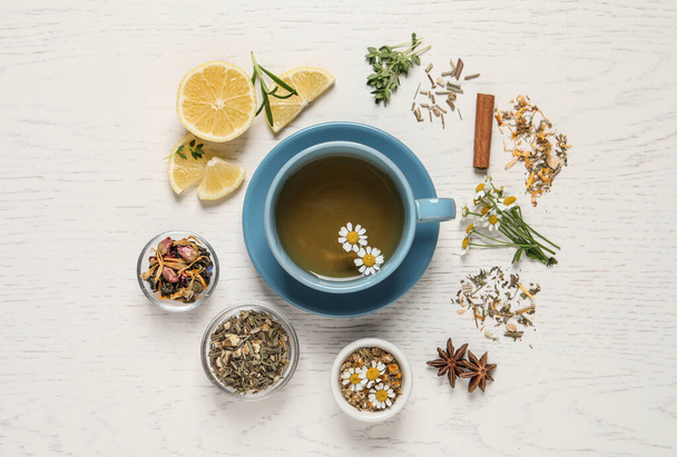 Flat lay composition of freshly brewed tea with chamomile flowers and dry leaves on white wooden table - Valokuva, kuva