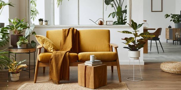 Interior design of scandinavian open space with yellow velvet sofa, plants, furniture, book, wooden cube and personal accessories in stylish home staging. Template. - Фото, изображение
