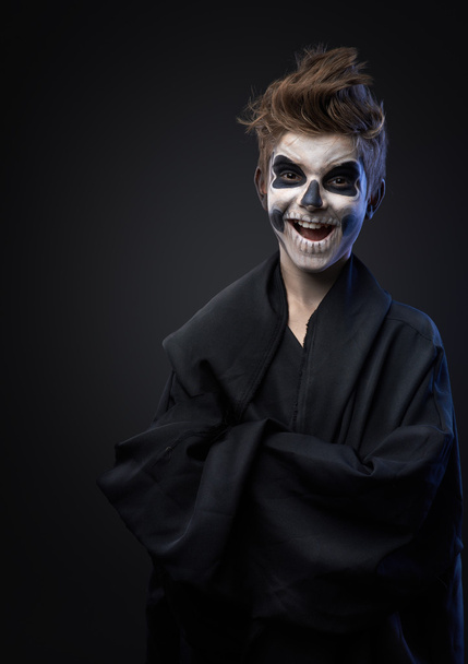 Teen with make-up of skull in black cloak laughs - Fotó, kép
