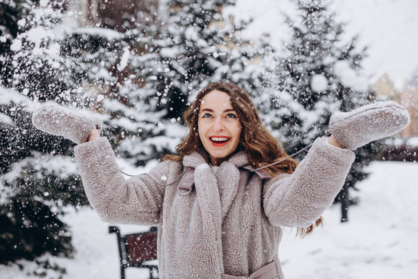 Πορτρέτο του χαριτωμένο κορίτσι που διασκεδάζει με το χιόνι στο πάρκο το χειμώνα φορώντας παλτό - Φωτογραφία, εικόνα