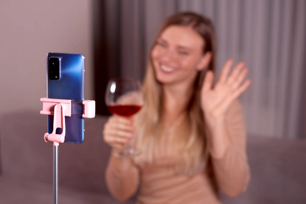 mujer sostiene un vaso de vino en la mano y las olas de la mano a la cámara del teléfono. enfoque selectivo, enfoque en primer plano, profundidad superficial de la foto de campo - Foto, Imagen