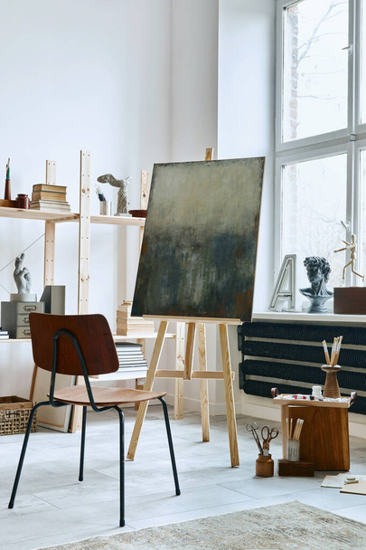Unique artist workspace interior with stylish teak commode, wooden easel, bookcase, artworks, painting accessories, decoration and elegant personal stuff. Modern work room for artist. Template. - Foto, Bild