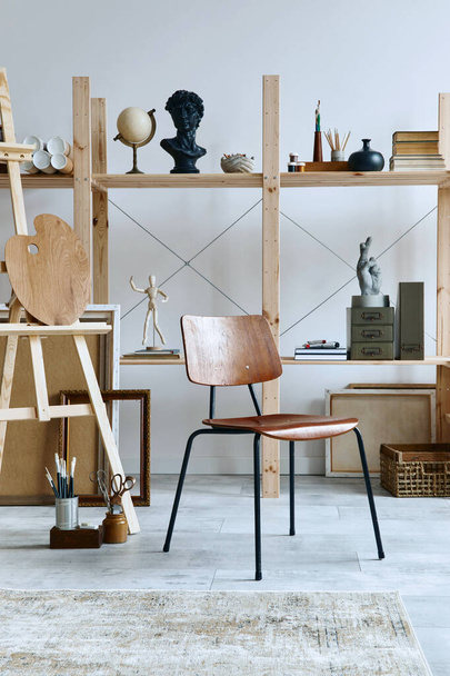 Unique artist workspace interior with stylish desk, wooden easel, bookcase, artworks, painting accessories, decoration and elegant personal stuff. Modern work room for artist. Template. - Фото, изображение
