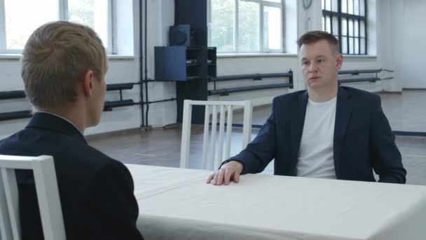 Nagranie dwóch mężczyzn siedzących naprzeciwko siebie w oczekiwaniu - Materiał filmowy, wideo