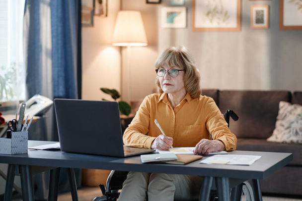 Rijpe vrouw die op laptop thuis werkt - Foto, afbeelding