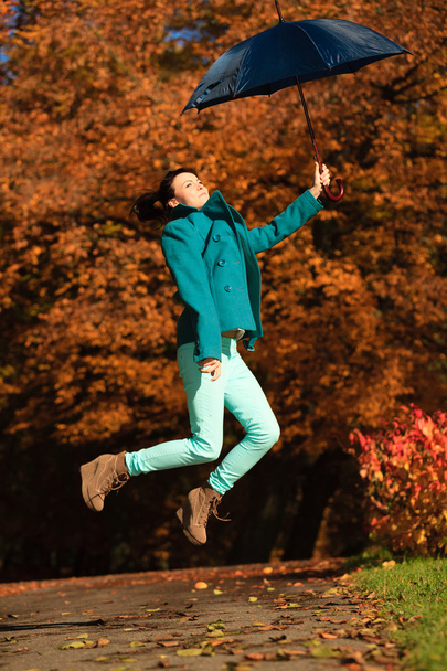 Girl jumping with blue umbrella in autumnal park - Foto, immagini