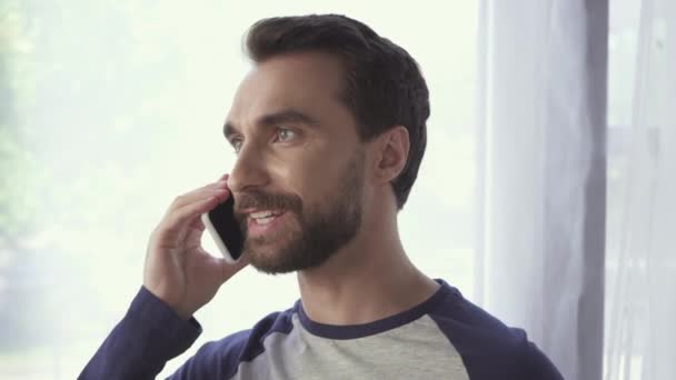 Positive bearded man talking on mobile phone at home  - Séquence, vidéo