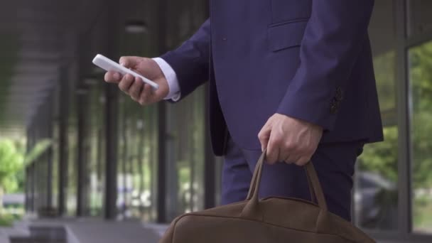 Przycięty widok biznesmena z torbą przy użyciu smartfona na zewnątrz  - Materiał filmowy, wideo