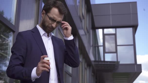 Empresario sosteniendo pastillas mientras sufre de dolor de cabeza al aire libre  - Metraje, vídeo