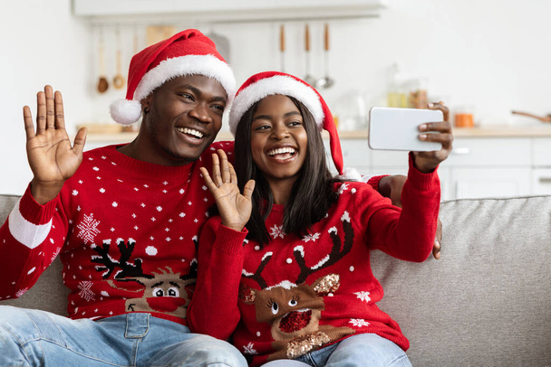 Beautiful black lovers in Santa hats waving at smartphone screen - Photo, Image