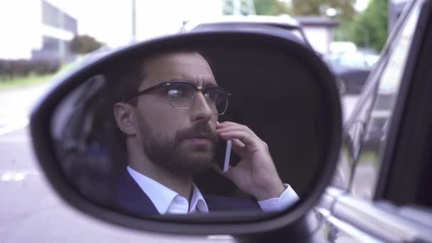 Empresario hablando por teléfono celular y reflejándose en el espejo del ala del coche  - Imágenes, Vídeo